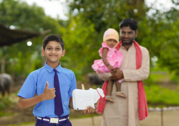 importance of saving concept : Smart indian little boy standing and holding piggy bank in hand with his father and little sister.
