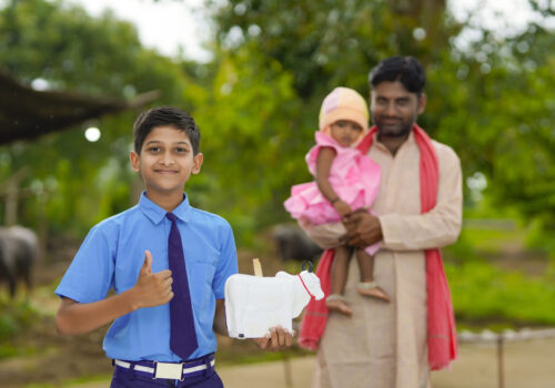 importance of saving concept : Smart indian little boy standing and holding piggy bank in hand with his father and little sister.